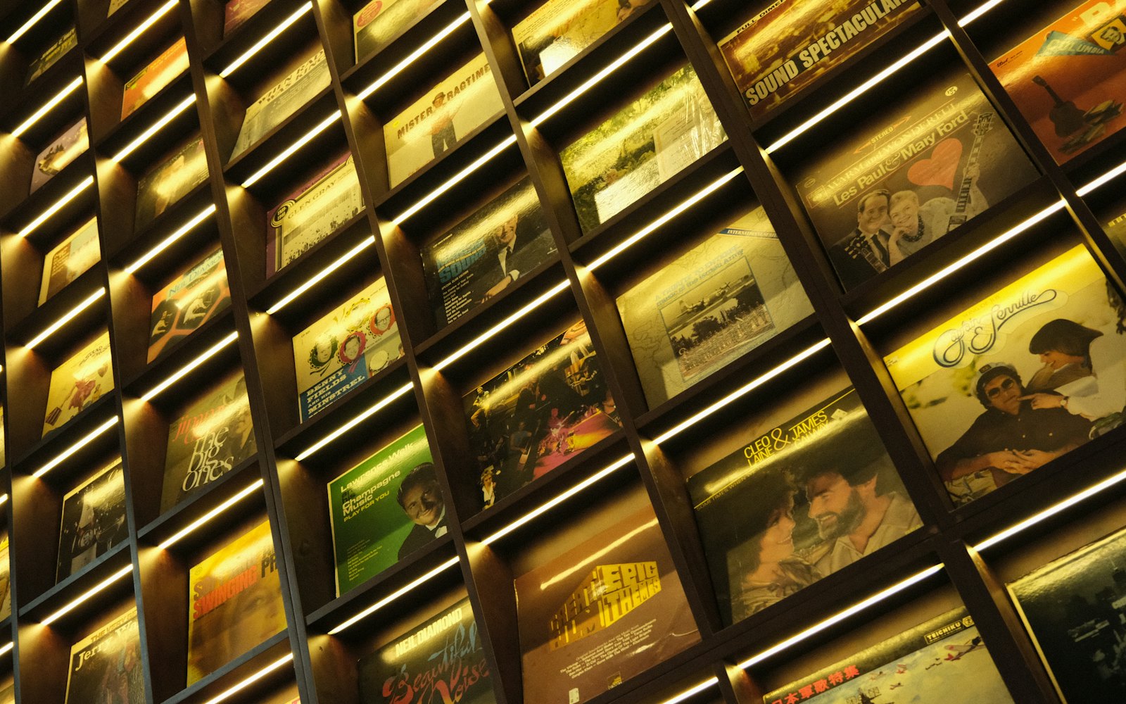 A wall of backlit vinyl record sleeves in a record shop