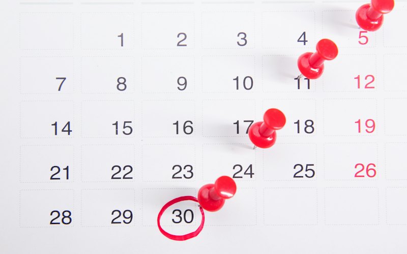 A wall calendar with red pushpins marching across the days of the month